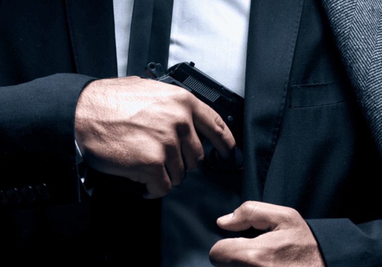 A man in a suit putting his concealed carry gun into his shoulder hoslter.