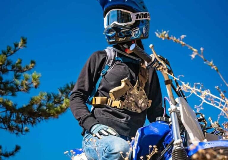 A man on a motor bike wearing a GunfightersINC Kenai Chest Holster.